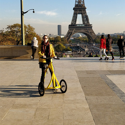 A rider crossing a plaza on their bright yellow Alinker walking bike